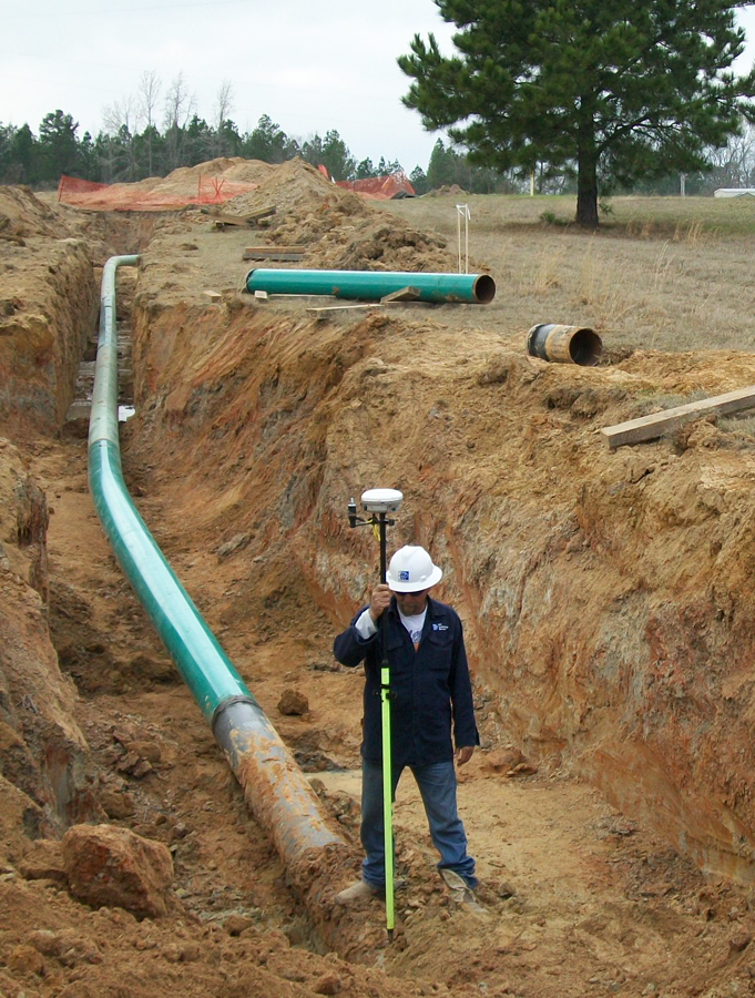 Surveyor using a GPS rover in a pipeline trench beside installed pipe